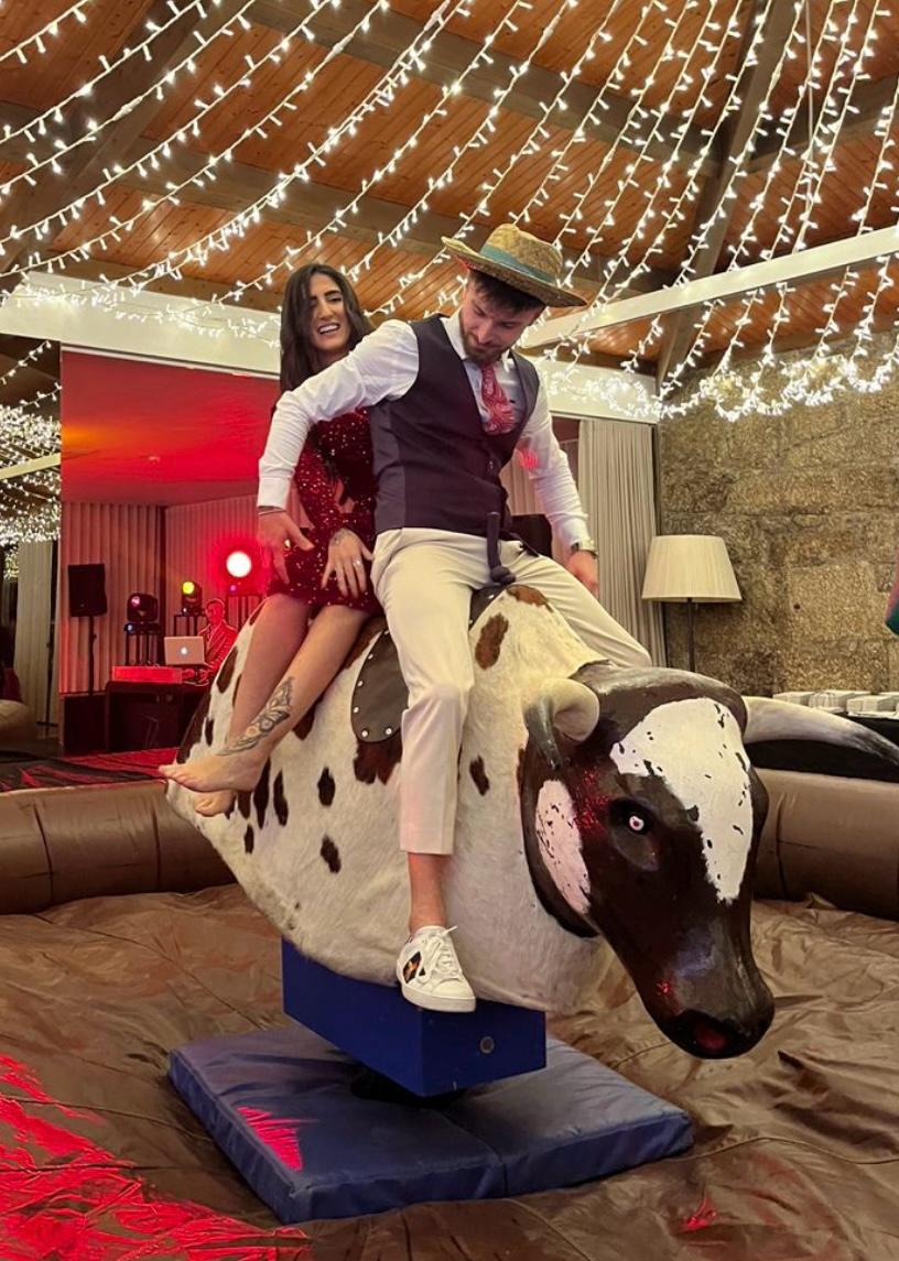 Casal a andar no touro mecânico na festa de casamento, sob luzes numa quinta